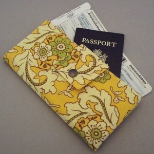 May include: A yellow floral fabric passport holder with a flap closure and a snap button. The holder has a passport, boarding pass, and a credit card inside.