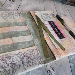 May include: A fabric journal cover featuring a vintage world map print in beige and muted green tones. The cover includes a green ribbon bookmark, a pen loop holding a black pen, and a white business card with the text www.dollbirdies.etsy.com.