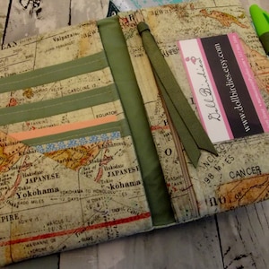 May include: A green fabric journal cover with a vintage world map design. The cover has multiple pockets and a green ribbon bookmark. The text "Doll Birdies" and "www.dollbirdies.etsy.com" is printed on a white card inside the cover.