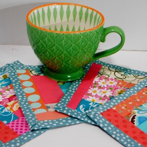 May include: Four colourful fabric coasters with a teal border and a green ceramic mug on top. The coasters are made of patchwork fabric with various patterns and colours, including pink, orange, blue, and white.