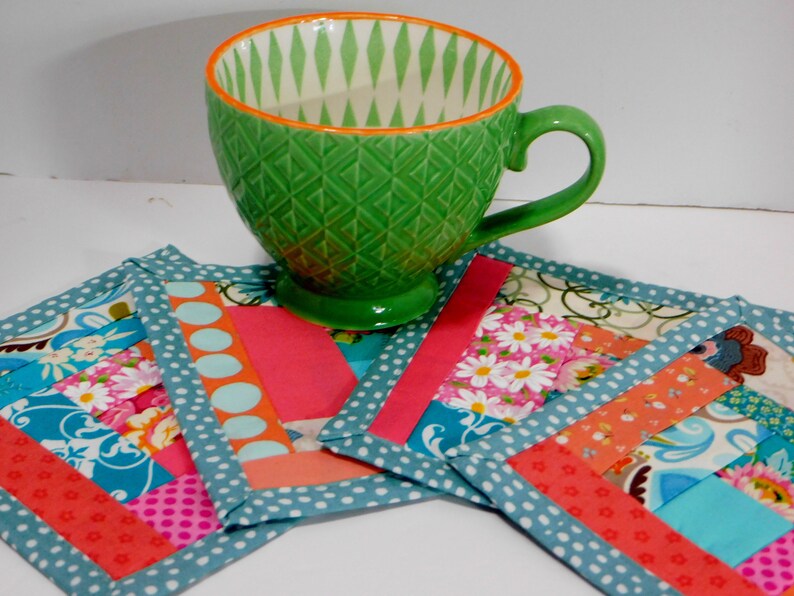 May include: Four colourful fabric coasters with a teal border and a green ceramic mug on top. The coasters are made of patchwork fabric with various patterns and colours, including pink, orange, blue, and white.