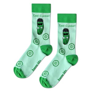 May include: A pair of novelty socks with a light green background and green accents. The socks feature a cartoon pickle wearing sunglasses and a cap, with the text "Cool-Cumber". Cucumber slices and the text "hanna hits" are also visible.