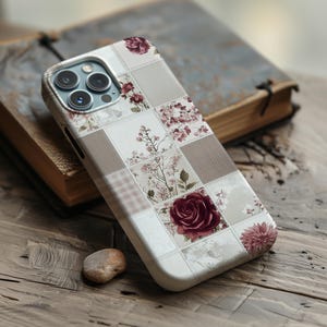 Könnte beinhalten: Eine Smartphone-Hülle mit einem Patchwork-Design aus abwechselnden Quadraten. Das Muster umfasst einfarbige beige und karierte Quadrate sowie Quadrate, die mit Illustrationen von dunkelroten Rosen, rosa Blüten und zarten Zweigen verziert sind.