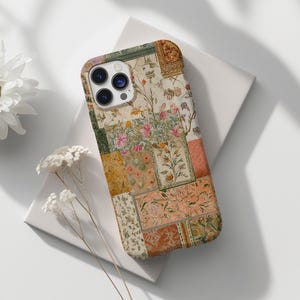 Könnte beinhalten: Eine Handyhülle mit Patchwork-Muster, das florale und geometrische Muster in Rosa-, Grün- und Goldtönen aufweist. Die Hülle hat eine rechteckige Form und ist für ein Smartphone konzipiert. Das Design erinnert an Vintage-Textilien.