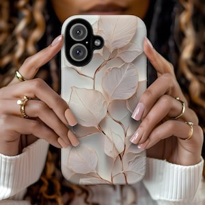 Puede incluir: Funda de teléfono blanca con un diseño de hojas y tallos beige. La funda tiene un recorte para una cámara de doble lente. Las hojas tienen una apariencia sutil y texturizada.