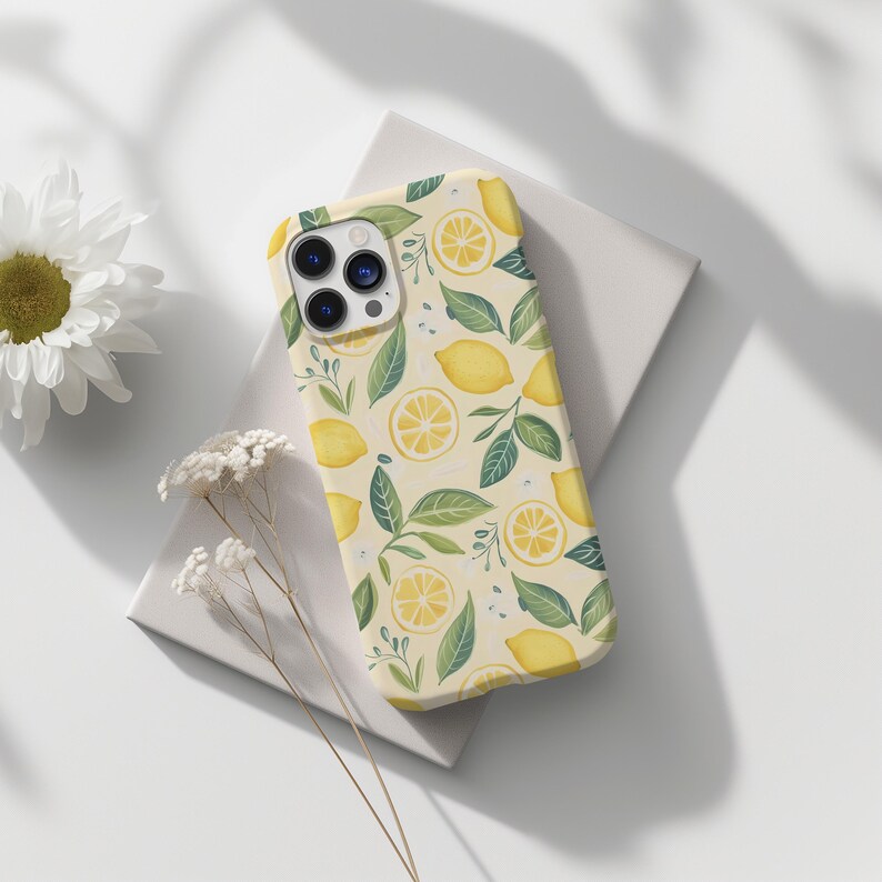 May include: A white phone case with a lemon and leaf pattern. The case has a camera lens cutout and a white background.