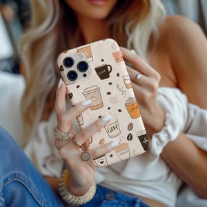 May include: A beige iPhone case with a white background and a pattern of coffee cups, coffee beans, and the word "COFFI" in a brown font.