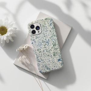 Pode incluir: Uma capa de telefone branca com um padrão floral em tons de azul e verde. A capa tem um recorte para a lente da câmera.