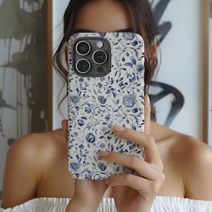 May include: A white phone case with a blue floral pattern. The case has a camera lens cutout and a raised lip around the edges.