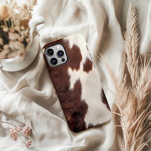 May include: A brown and white cowhide patterned phone case for an iPhone with a camera lens cutout.