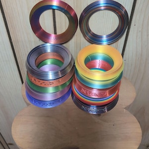 May include: A set of colorful, stacked rings with a rainbow pattern. The rings are made of plastic and have a smooth, glossy finish. The rings are labeled "Nick V" and "Rob V".