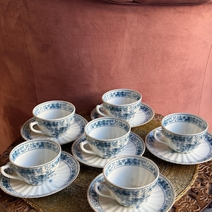 Puede incluir: Juego de seis tazas de té y platillos de porcelana azul y blanca con un patrón floral. Las tazas y los platillos tienen un diseño acanalado y un borde dorado.