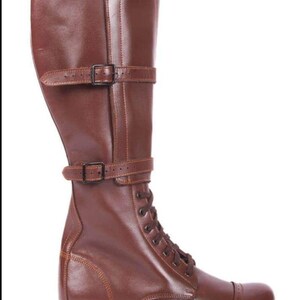 May include: Brown leather knee-high boots with a lace-up front and buckle straps. The boots have a rounded toe and a thick sole.