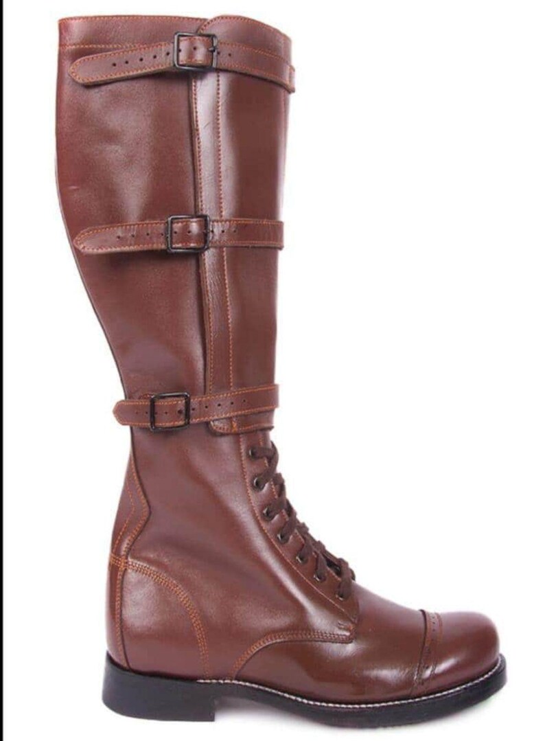 May include: Brown leather knee-high boots with a lace-up front and buckle straps. The boots have a rounded toe and a thick sole.