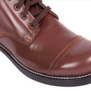 May include: Close-up of a brown leather boot with a lace-up closure and a white stitching detail around the sole.