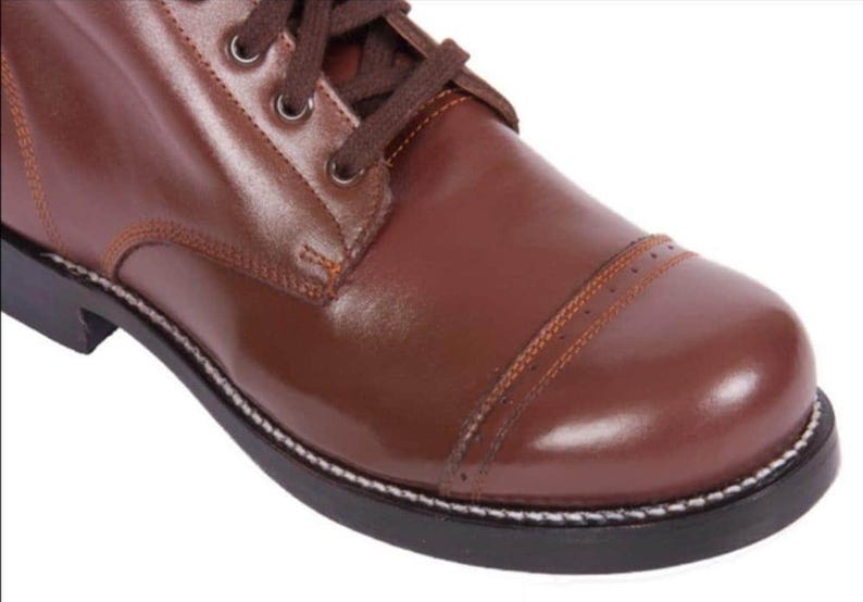 May include: Close-up of a brown leather boot with a lace-up closure and a white stitching detail around the sole.