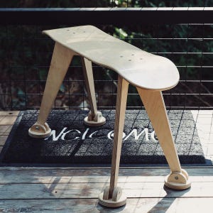 May include: A wooden stool made from a skateboard with a black welcome mat underneath.