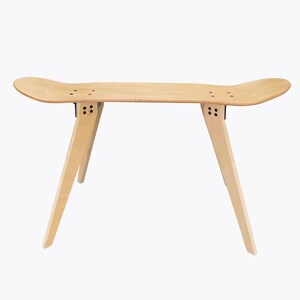 K&ouml;nnte beinhalten: Eine Holzbank aus einem Skateboard-Deck mit vier Beinen. Die Bank ist hellbraun und hat eine nat&uuml;rliche Holzoptik.