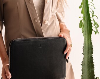 May include: A black leather laptop sleeve with a zipper closure. The sleeve has a small logo on the front.