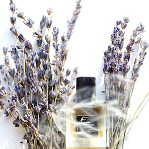 May include: A clear glass bottle of Lavender Noir botanical perfume with a black cap, surrounded by dried lavender flowers. The bottle label reads "Lavender Noir Botanical Perfume".