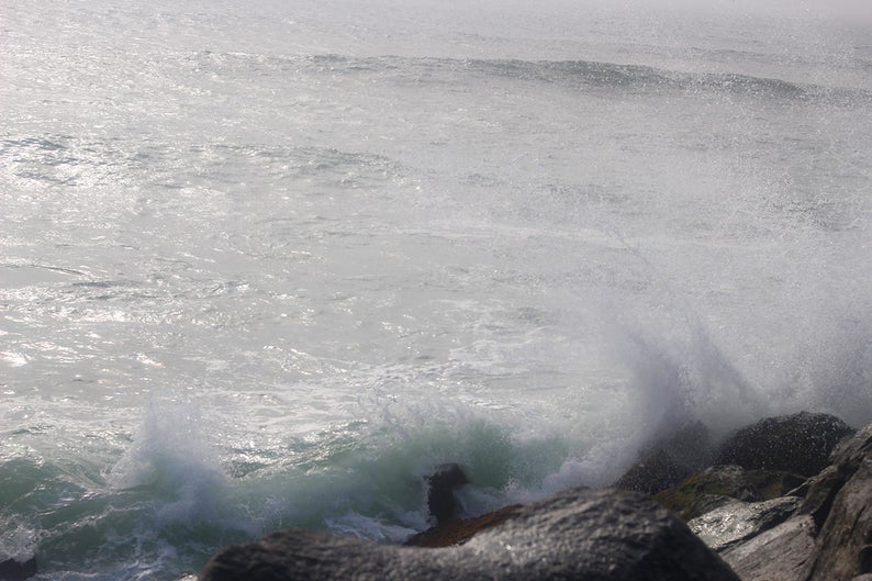 Pode incluir: Um close-up de uma costa rochosa com ondas quebrando. A &aacute;gua &eacute; de cor cinza claro e as rochas s&atilde;o de cor cinza escuro. As ondas criam um spray branco.