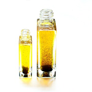 May include: Two clear glass bottles with square bases filled with a yellow liquid and dark flecks. The bottles are different sizes.