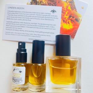 Peut inclure: Deux flacons de parfum botanique Linden Moon en verre, l'un avec un bouchon noir et l'autre avec un bouchon transparent. Les flacons sont pos&eacute;s sur une surface blanche avec une carte qui indique "Linden Moon" et d&eacute;crit le parfum comme un "m&eacute;lange sensuel et r&ecirc;veur qui d&eacute;gage la chaleur de l'&eacute;t&eacute;."