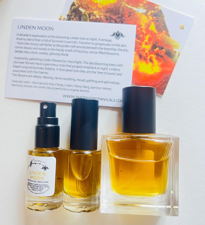 Peut inclure: Deux flacons de parfum botanique Linden Moon en verre, l'un avec un bouchon noir et l'autre avec un bouchon transparent. Les flacons sont pos&eacute;s sur une surface blanche avec une carte qui indique "Linden Moon" et d&eacute;crit le parfum comme un "m&eacute;lange sensuel et r&ecirc;veur qui d&eacute;gage la chaleur de l'&eacute;t&eacute;."