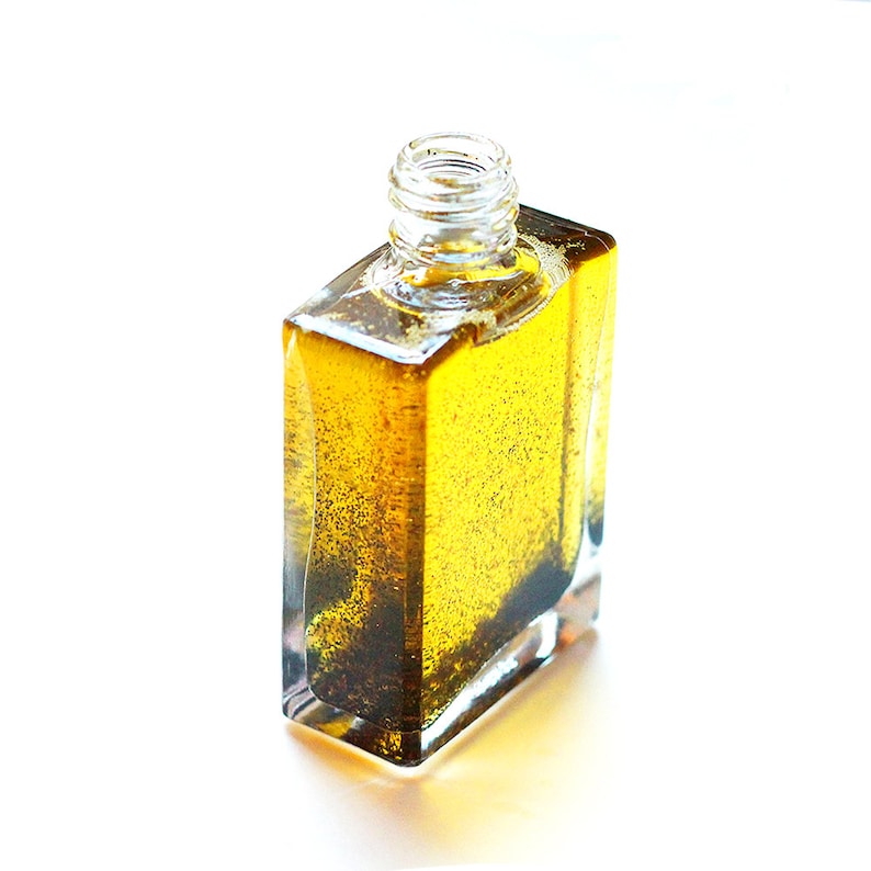 May include: A clear glass bottle filled with a golden yellow liquid. The bottle has a square shape and a textured surface.