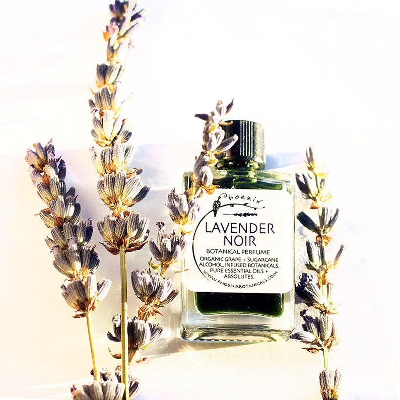 May include: A small glass bottle of lavender noir botanical perfume with a green label that reads "Phoenix Lavender Noir Botanical Perfume Organic Grape Sugarcane Alcohol Infused Botanicals Pure Essential Oils Absolutes www.phoenixbotanicals.com".