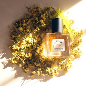 Peut inclure: Un petit flacon de parfum botanique Linden Moon en verre avec un bouchon noir. Le flacon est entour&eacute; de fleurs jaunes.