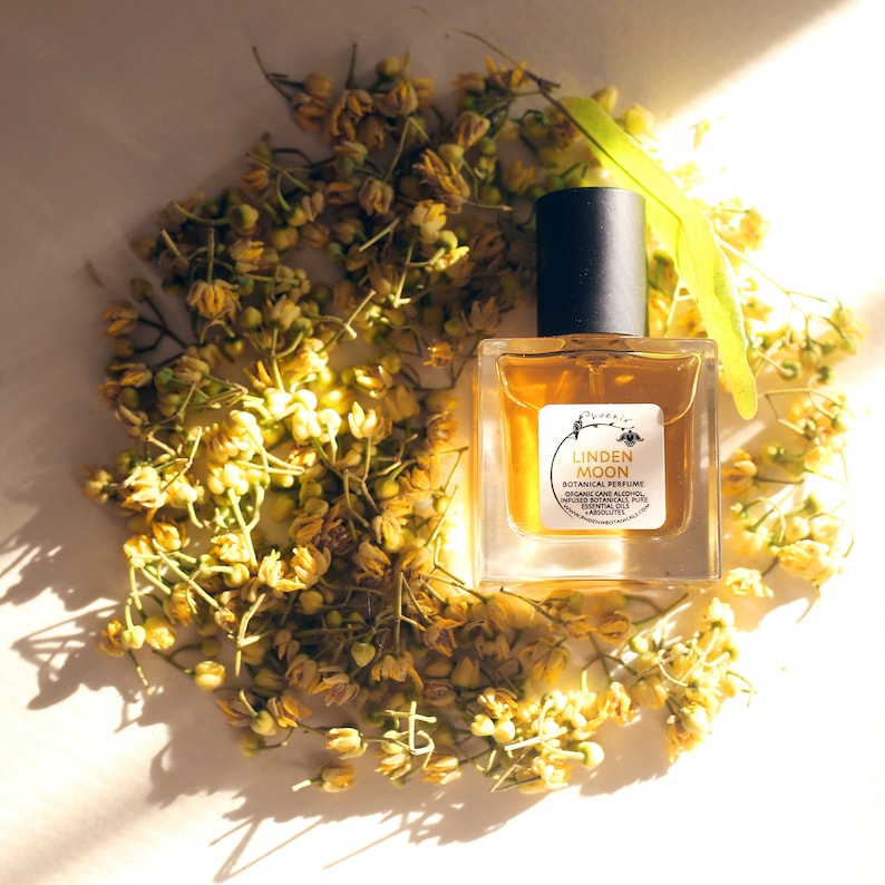 Peut inclure: Un petit flacon de parfum botanique Linden Moon en verre avec un bouchon noir. Le flacon est entour&eacute; de fleurs jaunes.