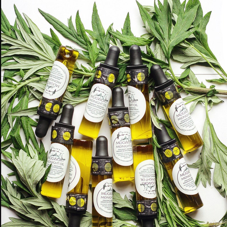 Pode incluir: Uma cole&ccedil;&atilde;o de dez pequenos frascos de vidro cheios de um l&iacute;quido amarelo claro. Os frascos t&ecirc;m conta-gotas pretos e etiquetas brancas com o texto "Mugwort Midnight Oil" impresso neles. Os frascos est&atilde;o dispostos sobre uma superf&iacute;cie branca cercada por folhas verdes.