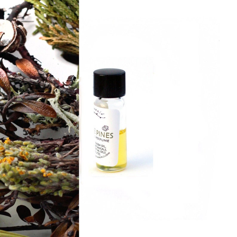 May include: A small glass bottle with a black cap filled with a yellow liquid. The bottle has a white label with the text "PINES PERFUME" and "JOJOBA OIL, BOTANICALS & ESSENTIAL OILS, WWW.BOTANICALS.COM".