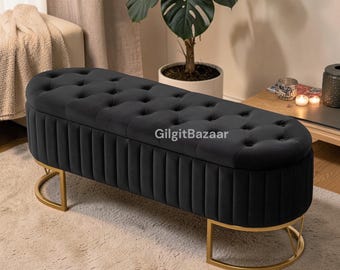 Banco otomano de terciopelo negro con espacio de almacenamiento, cabecero de cama capitoné y patas de metal dorado.
