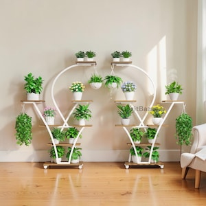 May include: Two white metal plant stands with multiple wooden shelves, each holding various potted plants and hanging baskets. The stands have a curved design and are placed on a wooden floor. The plants include green foliage and flowering plants.