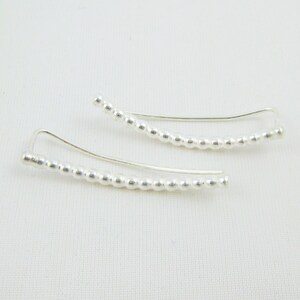 May include: A pair of silver ear cuffs with a beaded design. The cuffs are curved and have a simple, minimalist style.