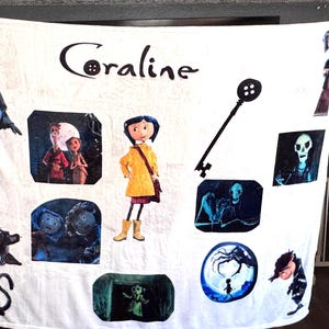 May include: White Coraline-themed blanket featuring various character illustrations and the movie title. The design includes images of Coraline, the black cat, and other characters from the animated film. A key graphic is also present.