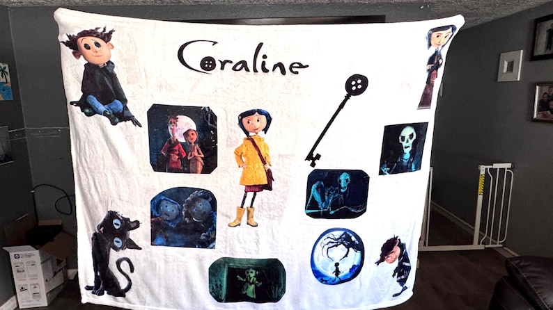 May include: White Coraline-themed blanket featuring various character illustrations and the movie title. The design includes images of Coraline, the black cat, and other characters from the animated film. A key graphic is also present.