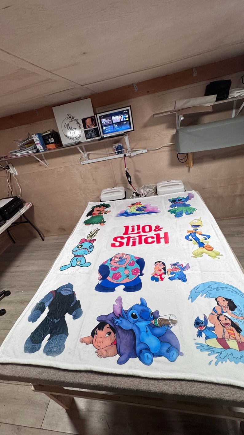 May include: White blanket featuring colorful cartoon characters from Lilo & Stitch. The blanket has the words "Lilo & Stitch" in red and white. Various characters are depicted in blue, pink, and green.