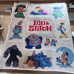 May include: A large, off-white blanket featuring multiple colorful images of characters from the animated film "Lilo & Stitch." The blanket has a large central text that reads "Lilo & Stitch" in red and white. The blanket is rectangular.