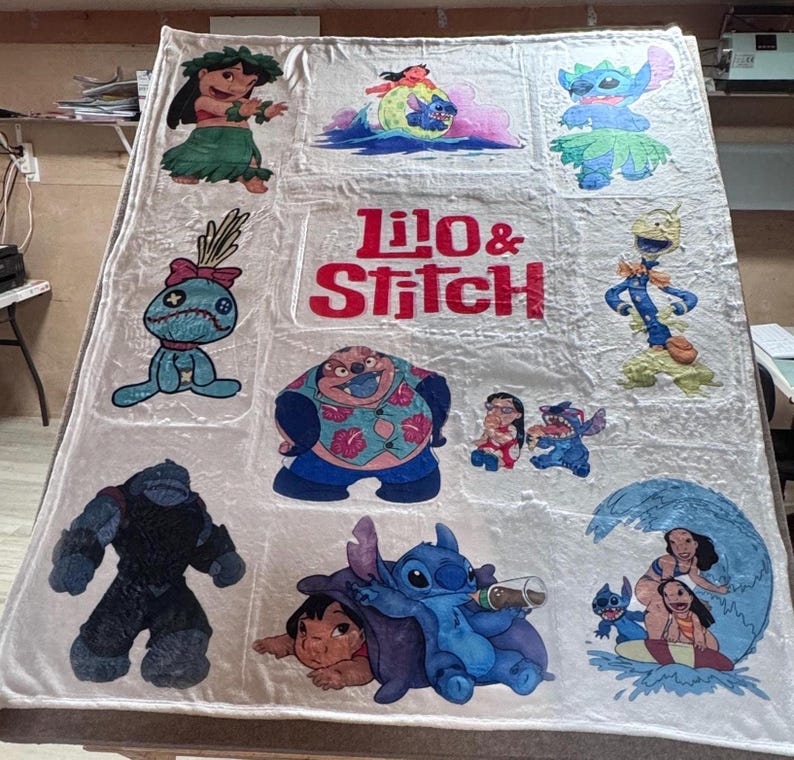May include: A large, off-white blanket featuring multiple colorful images of characters from the animated film "Lilo & Stitch." The blanket has a large central text that reads "Lilo & Stitch" in red and white. The blanket is rectangular.
