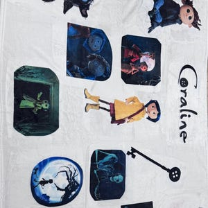 May include: White blanket featuring multiple images from the movie "Coraline." The images include a black cat, characters, and scenes from the film. The word "Coraline" is written in black script on the blanket.