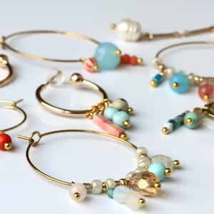 May include: A set of gold hoop earrings with colourful beads and charms. The earrings feature a variety of beads, including turquoise, white, pink, and red. The charms include small gold beads and a few larger beads with a textured surface.