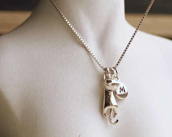Puede incluir: Un collar de cadena de plata con un dije de plata de un gato y un dije de disco de plata con la letra "M" grabada en él.