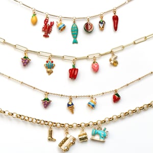 Op de afbeelding: Vier gouden kettingen met kleurrijke emaille-charms. De charms omvatten een kreeft, een vis, een watermeloen, een citroen, een peper, een aardbei, een ijsje, een laars, een naaimachine en andere ontwerpen.