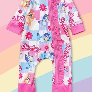 Może przedstawiać: R&oacute;żowo-biały pajacyk dla dziecka z postaciami z kresk&oacute;wek i napisem "Besties". Pajacyk ma zamek błyskawiczny z przodu, r&oacute;żowe falbanki i zakryte stopy. Wz&oacute;r zawiera postacie z kresk&oacute;wek, kwiaty i wz&oacute;r w szachownicę.