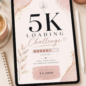 May include: A digital tablet shows a "5K Loading Challenge" graphic with a pink and gold design. The text includes "Small Steps Today, Big Freedom Tomorrow" and "Save Your First £3,900." A white stylus and a cup of coffee are next to the tablet.