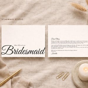 Può includere: Due biglietti color crema con calligrafia nera. Un biglietto recita "Olivia, Will you be my Bridesmaid" in elegante corsivo. Il secondo biglietto contiene una lettera scritta a mano. La scena comprende una penna dorata, graffette, una candela e un piccolo vaso con fiori secchi.
