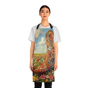 May include: A colorful apron with a floral design featuring a cowboy boot in a field of flowers. The boot is decorated with flowers and has a blue sky and clouds in the background.